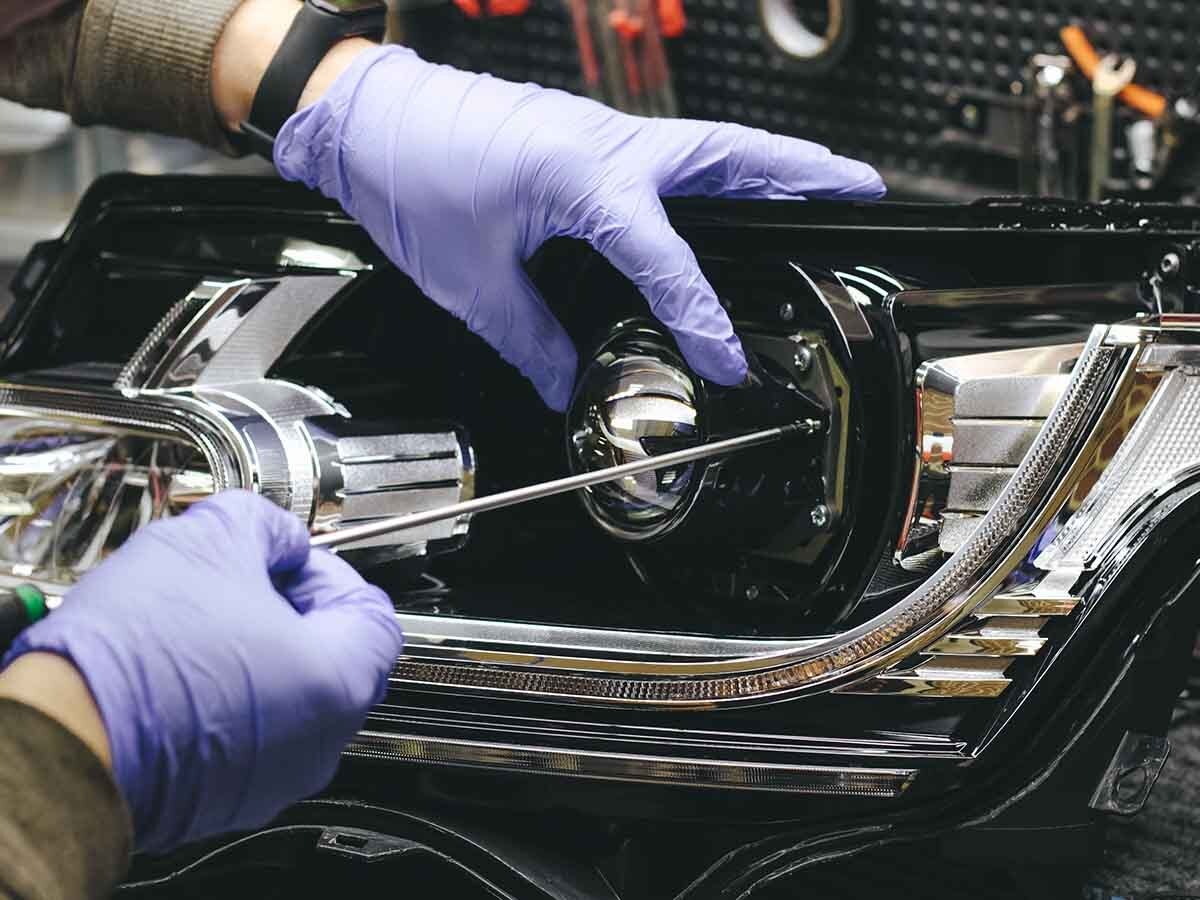 A mechanic is working on a car's projector headlights