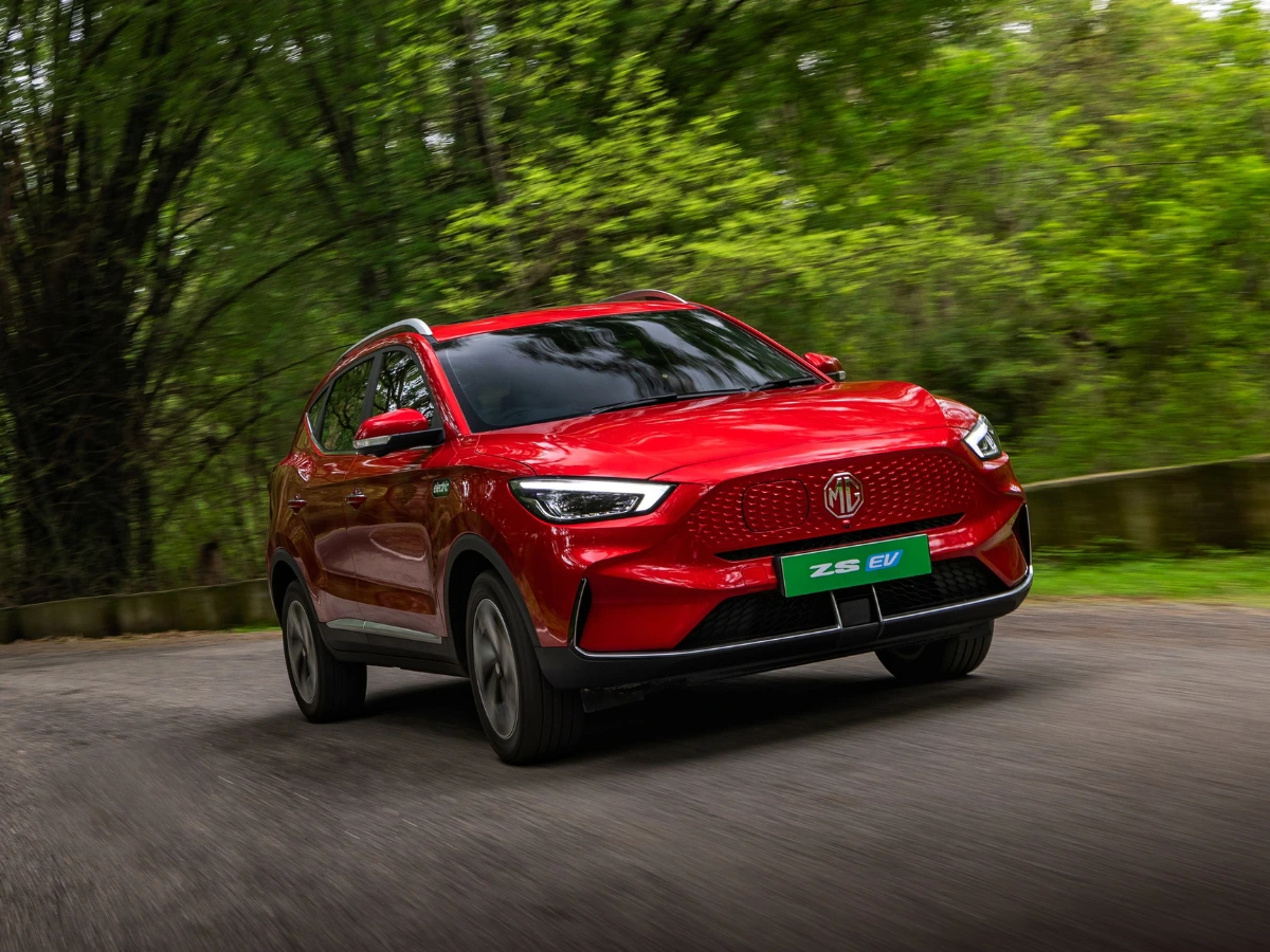 2026 MG ZS EV electric SUV in red driving on a scenic road, featuring its closed grille, LED headlights, and updated design