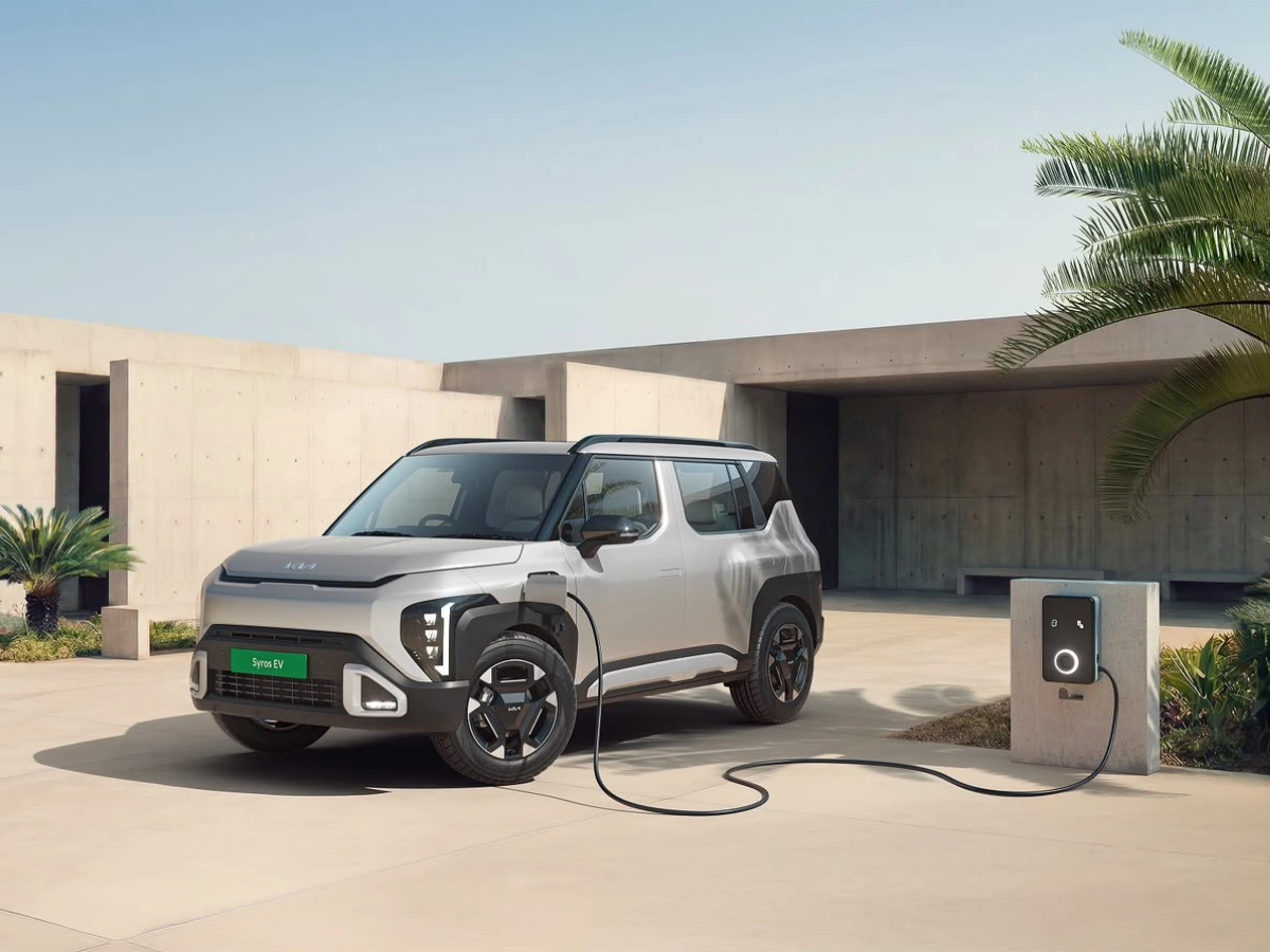 Silver Kia Syros EV charging, shown in a front three-quarter profile outside a modern residence