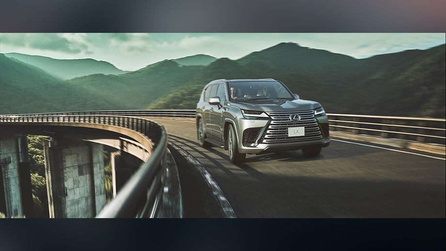 front view of a Atomic Silver Lexus LX driving on a curved bridge