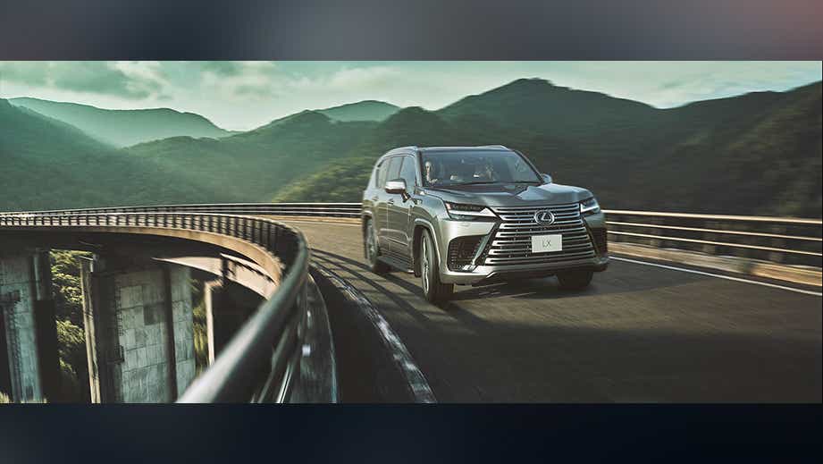 front view of a Atomic Silver Lexus LX driving on a curved bridge