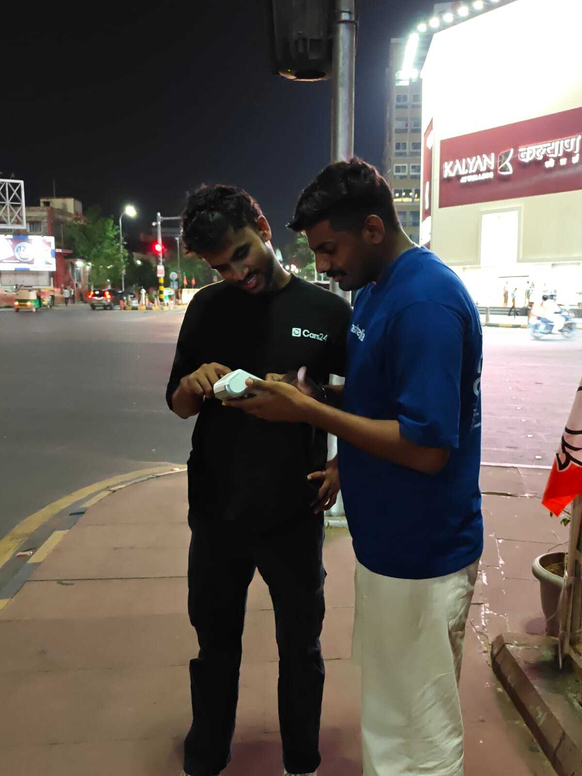 Cars24 and Crashfree India team members using a handheld SATARK device at night on a street in Jaipur.