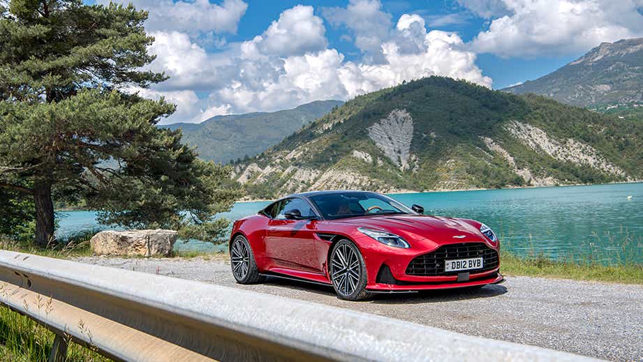 front three-quarter view of an Aston Martin DB12 by a lake with mountains in background