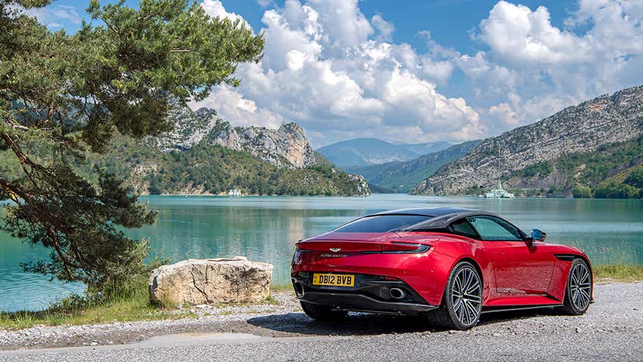 Rear three-quarter view of an Aston Martin DB12 by a lake and mountains