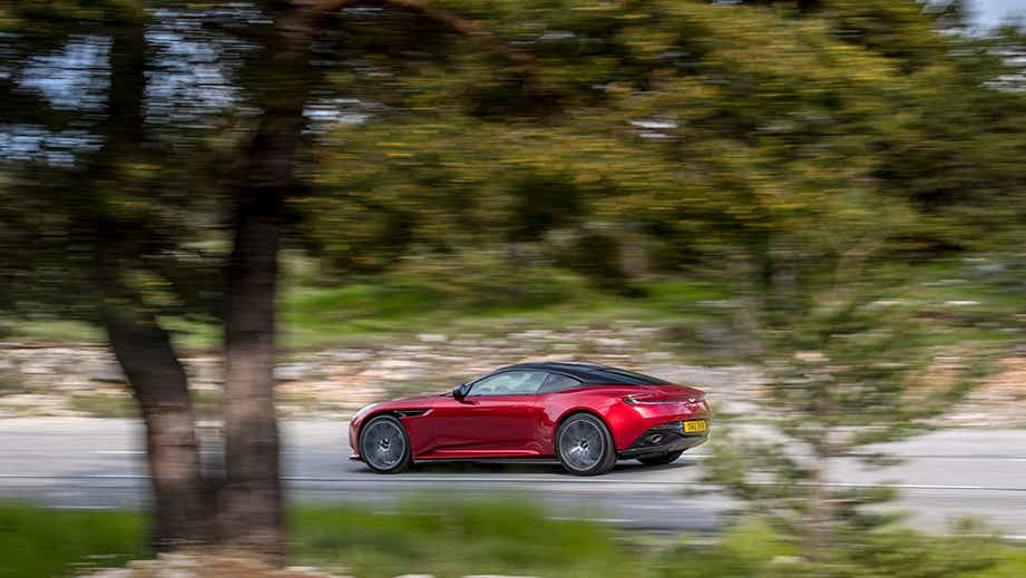 side view of an Aston Martin DB12 driving on a road
