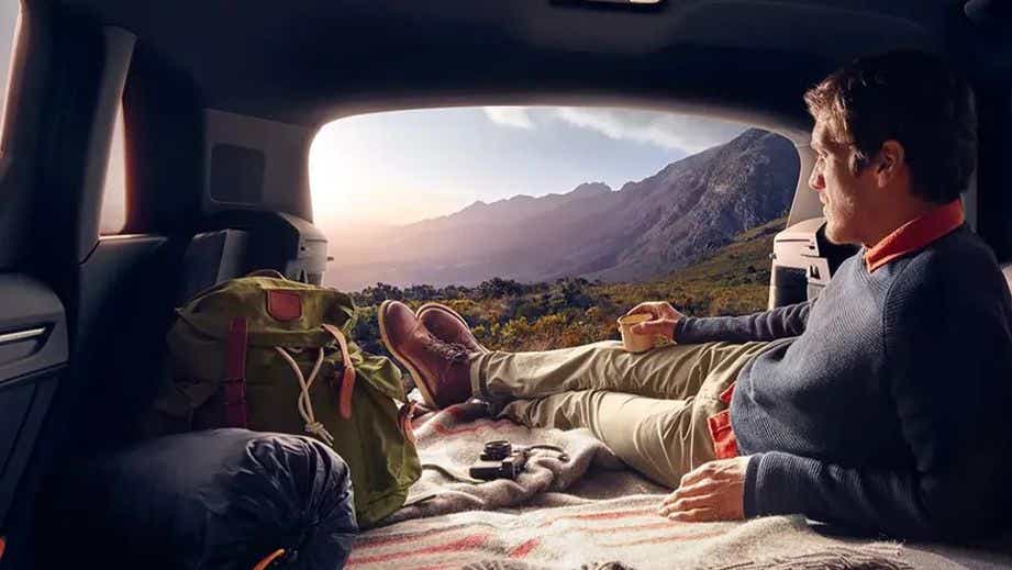 interior cargo area view of a Audi Q3 with a person relaxing, blanket and bags, mountain landscape through rear window