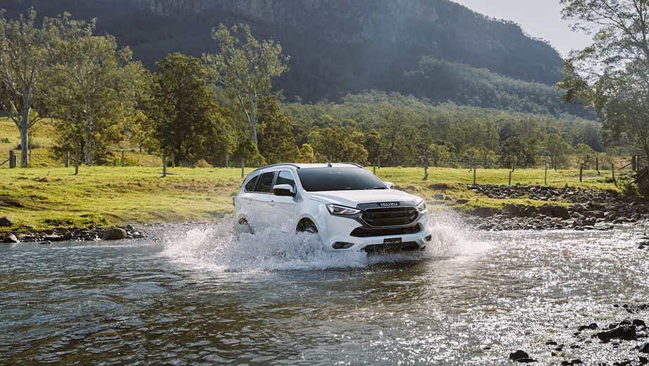 front three-quarter view of an Isuzu MU-X driving through a river