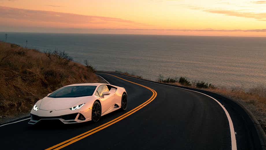 front three-quarter view of a Bianco Asopo Lamborghini Huracan Evo on a coastal road at sunset