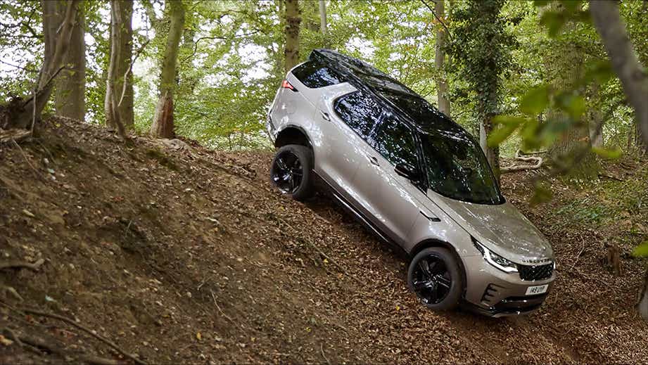 side view of a Land Rover Discovery driving off-road on a steep forest slope