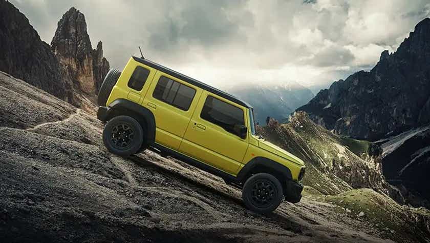 side view of a Kinetic Yellow With Bluish Black Roof Maruti Suzuki Jimny climbing a mountain slope