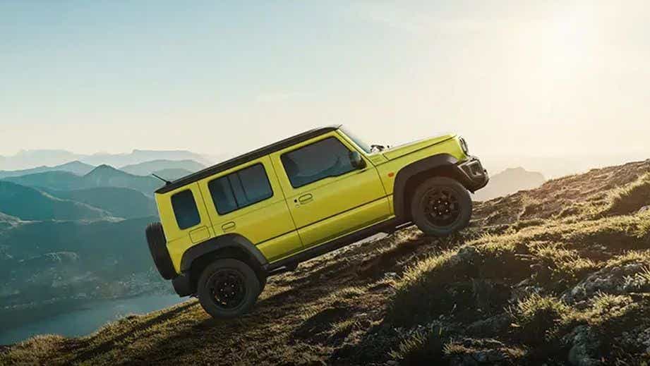 side view of a Kinetic Yellow With Bluish Black Roof Maruti Suzuki Jimny climbing a hill