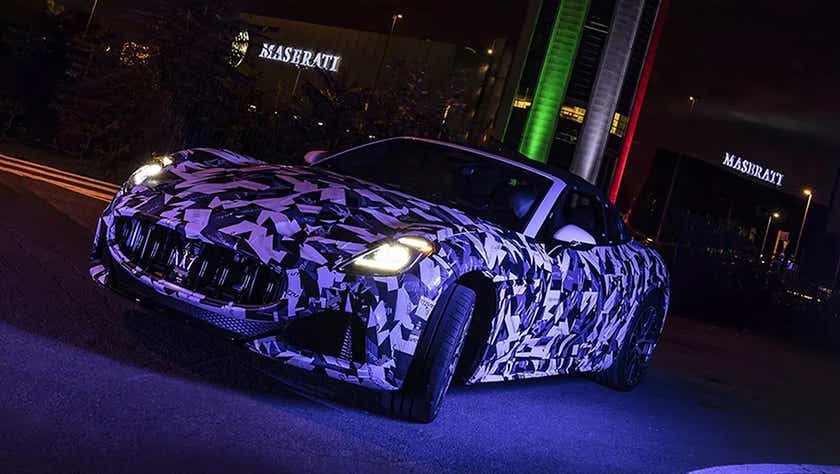 Front three-quarter view of a Maserati GranCabrio near Maserati building at night