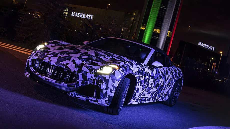 Front three-quarter view of a Maserati GranCabrio near Maserati building at night