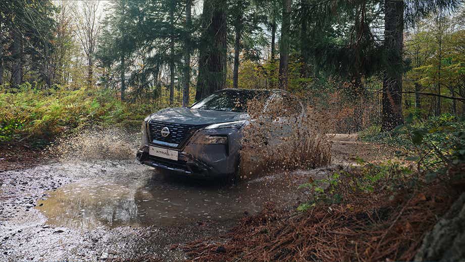 Front view of a Nissan X-Trail driving through a mud puddle in a forest