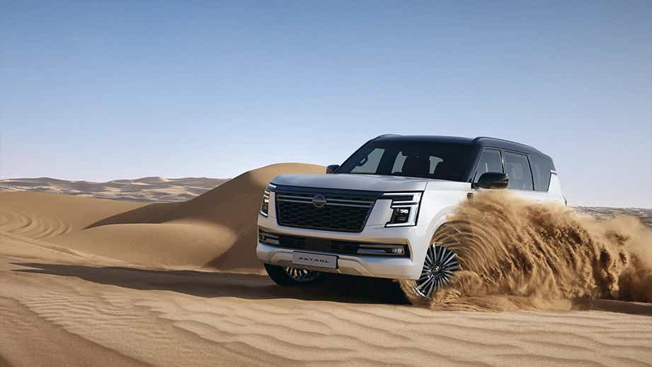 front three-quarter view of a Nissan Patrol driving over sand dunes