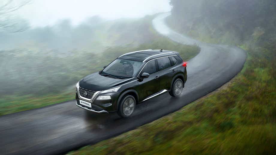 front three-quarter view of a Nissan X-Trail on a winding misty road