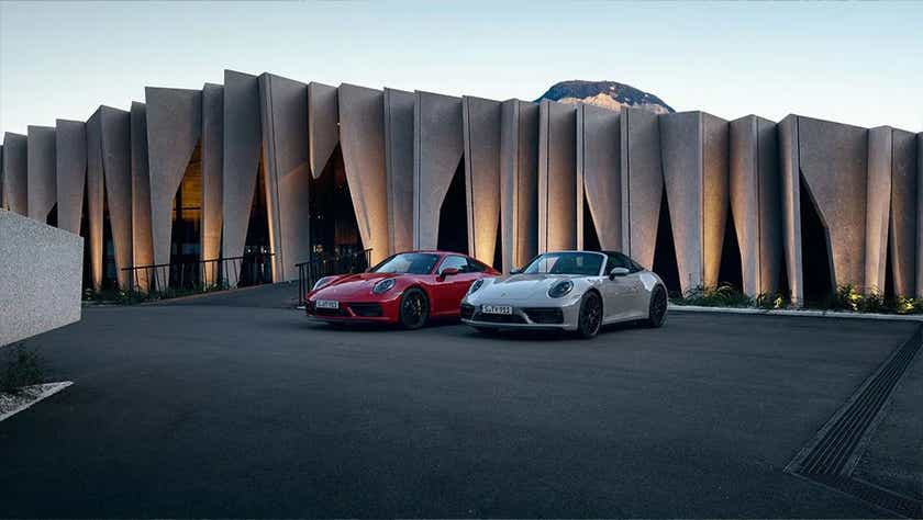 Front view of two Porsche 911 cars parked outside a modern building