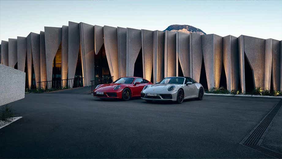Front view of two Porsche 911 cars parked outside a modern building