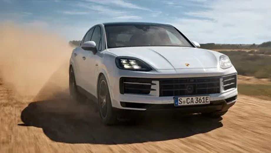 Front view of a Carrara White Metallic Porsche Cayenne Coupe driving on a dirt road