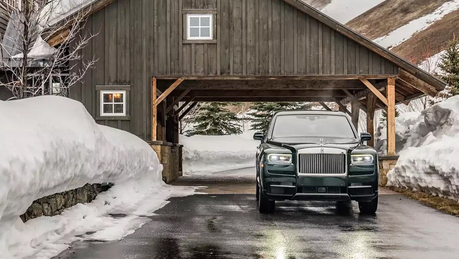 Front view of a Rolls-Royce Cullinan parked in snow outside a wooden building