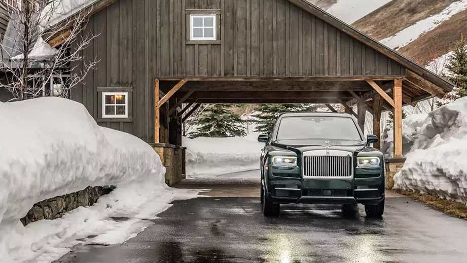 Front view of a Rolls-Royce Cullinan parked in snow outside a wooden building