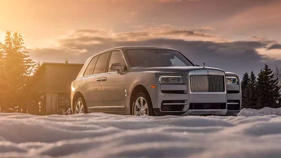 front three-quarter view of a Rolls-Royce Cullinan on snow at sunset