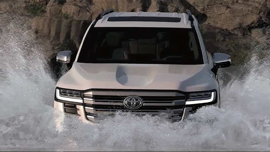 front view of a Precious White Pearl Toyota Land Cruiser 300 driving through water