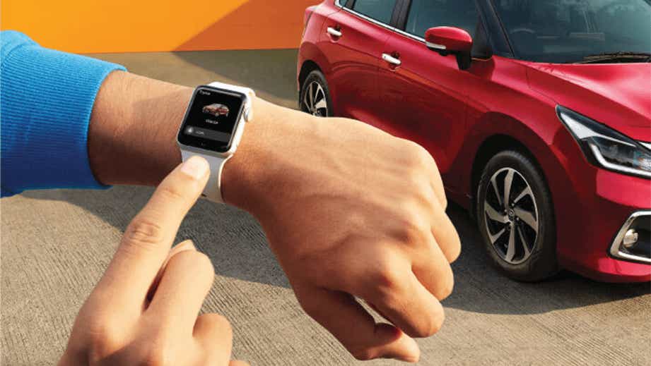 front-side view of a Toyota Glanza next to a person using a smartwatch
