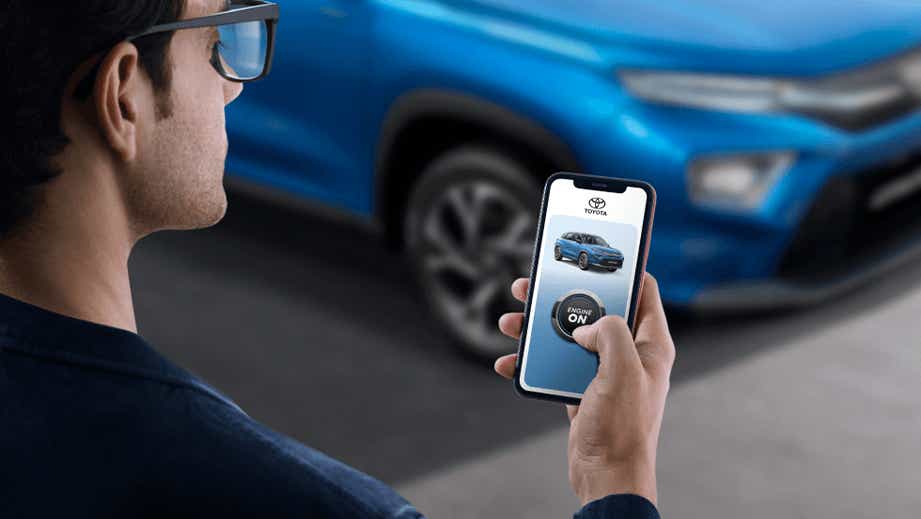 Man using a smartphone to start a Toyota Urban Cruiser Hyryder parked nearby