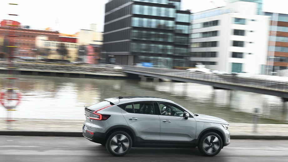 side view of a Volvo C40 Recharge driving near water with city buildings