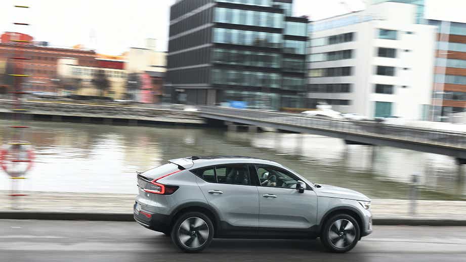 side view of a Volvo C40 Recharge driving near water with city buildings