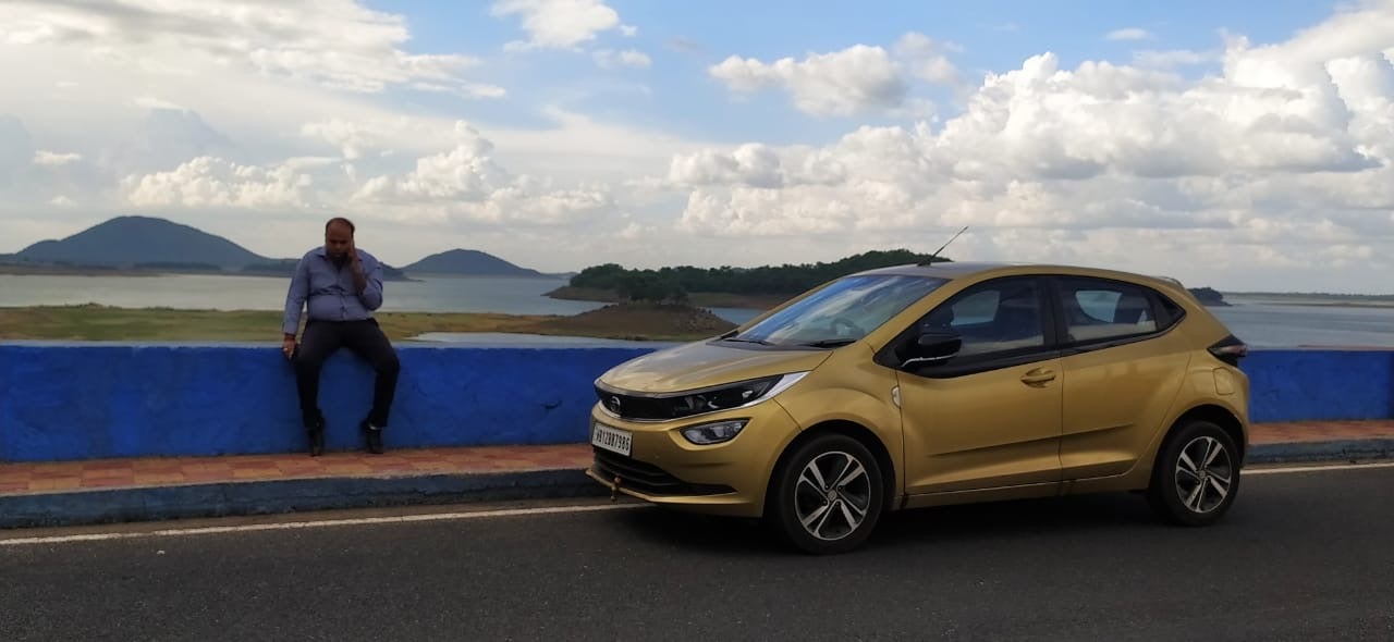 side view of a High Street Gold Tata Altroz 2020-2024 on a road by a scenic water body