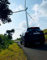 rear view of a Tata Harrier 2019-2023 on a rural road with a wind turbine