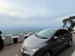 front three-quarter of a Honda City parked by a hill viewpoint