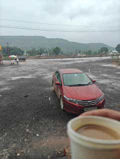 front three-quarter view of a Honda City in an open parking lot on a rainy day