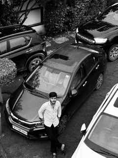 Top view of a Honda City with a person leaning on the front, parked outdoors