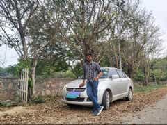 Front view of a Maruti Suzuki Dzire with a person standing beside it