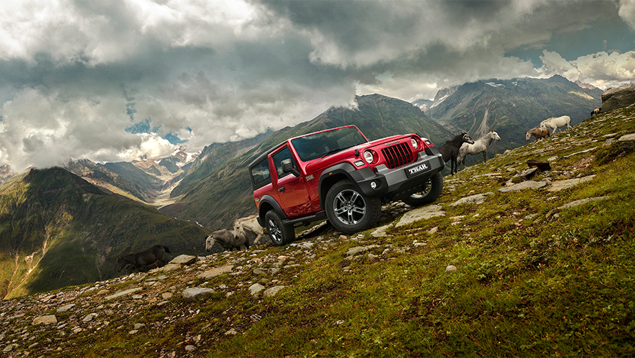 Front three-quarter view of a tango-red Mahindra Thar on a rocky mountain slope