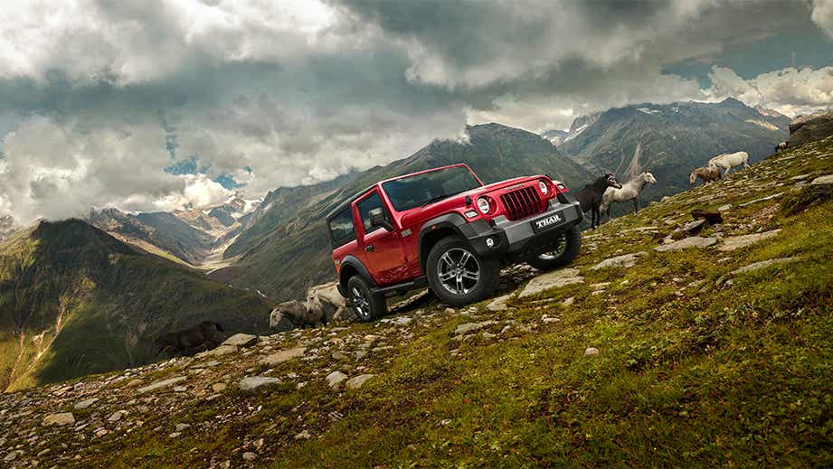 Front three-quarter view of a tango-red Mahindra Thar on a rocky mountain slope