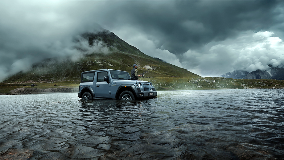 Side view of a galaxy grey Mahindra Thar in a mountain river