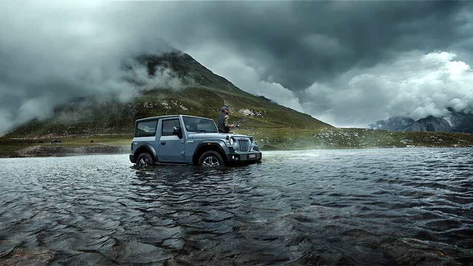 Side view of a galaxy grey Mahindra Thar in a mountain river
