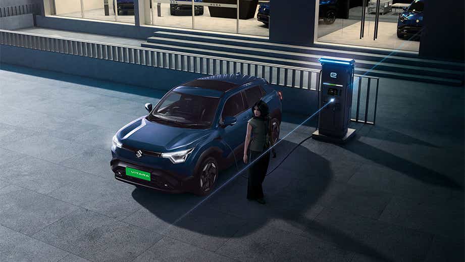 Front three-quarter view of a Nexa Blue Maruti Suzuki e Vitara charging at a station