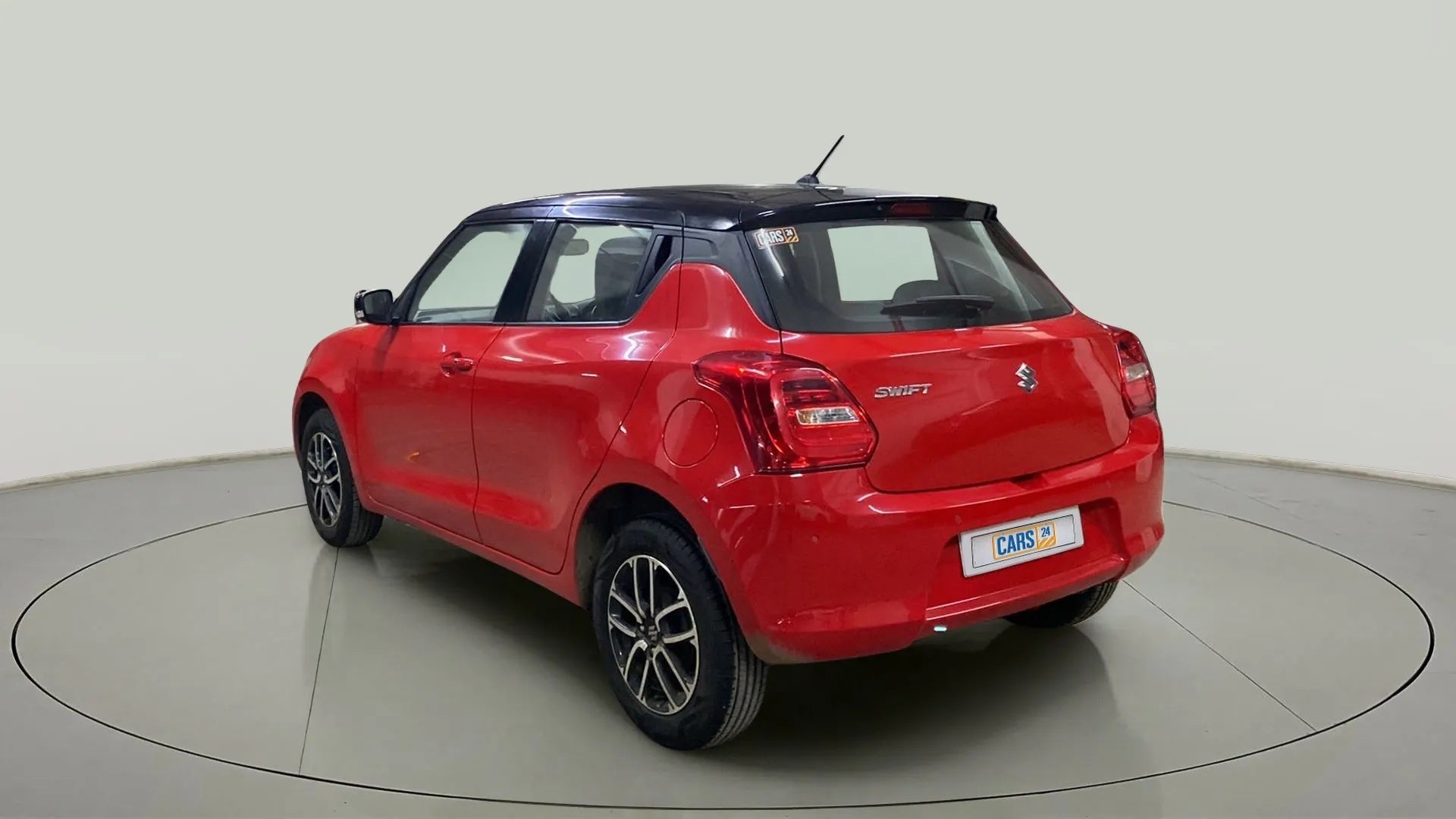 Rear three-quarter view of a solid fire red with pearl midnight black roof Maruti Suzuki Swift 2021 - 2023