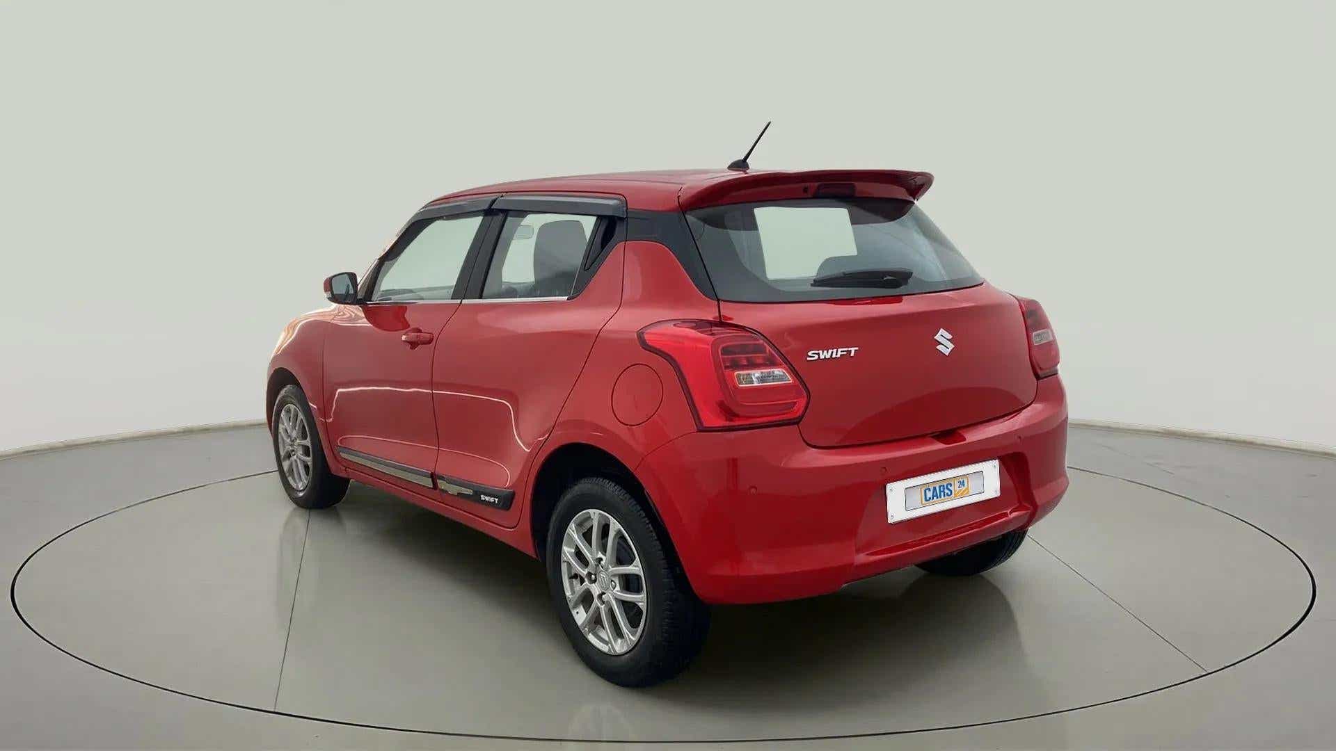 Rear three-quarter view of a solid fire red with pearl midnight black roof Maruti Suzuki Swift 2021 - 2023