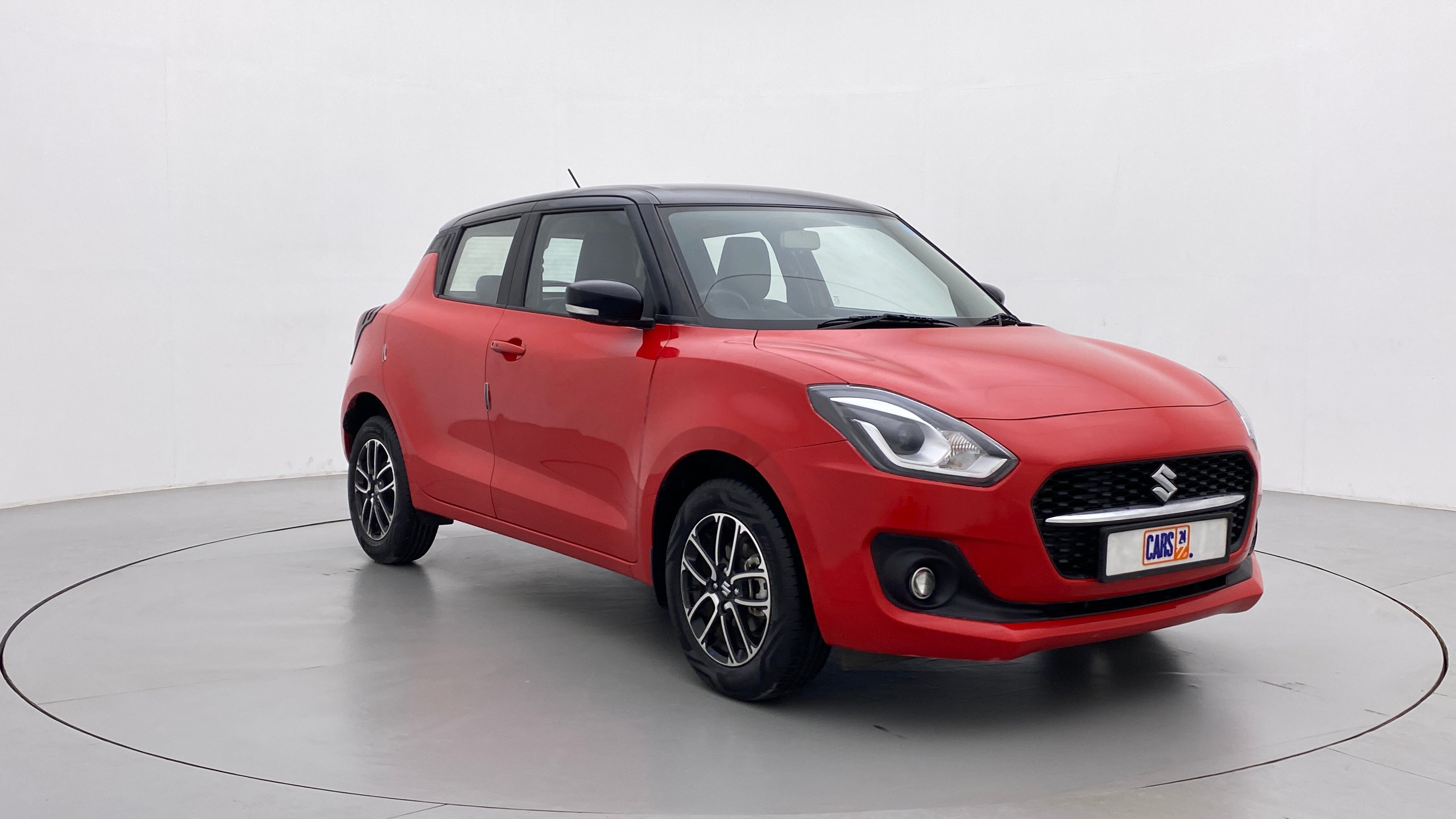 Front three-quarter view of a solid fire red with pearl midnight black roof Maruti Suzuki Swift 2021 - 2023
