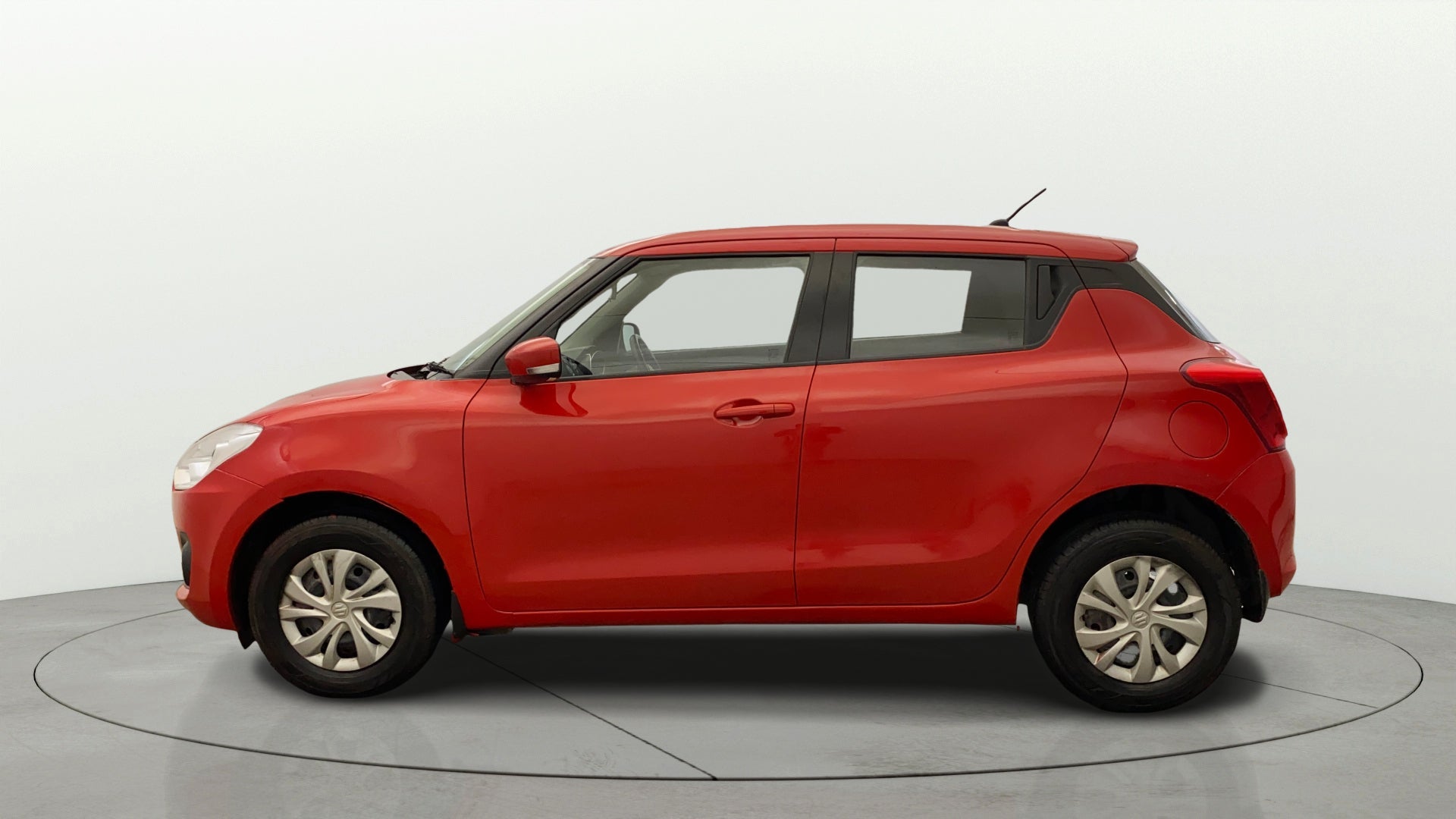 Side view of a solid fire red Maruti Suzuki Swift 2021 - 2023