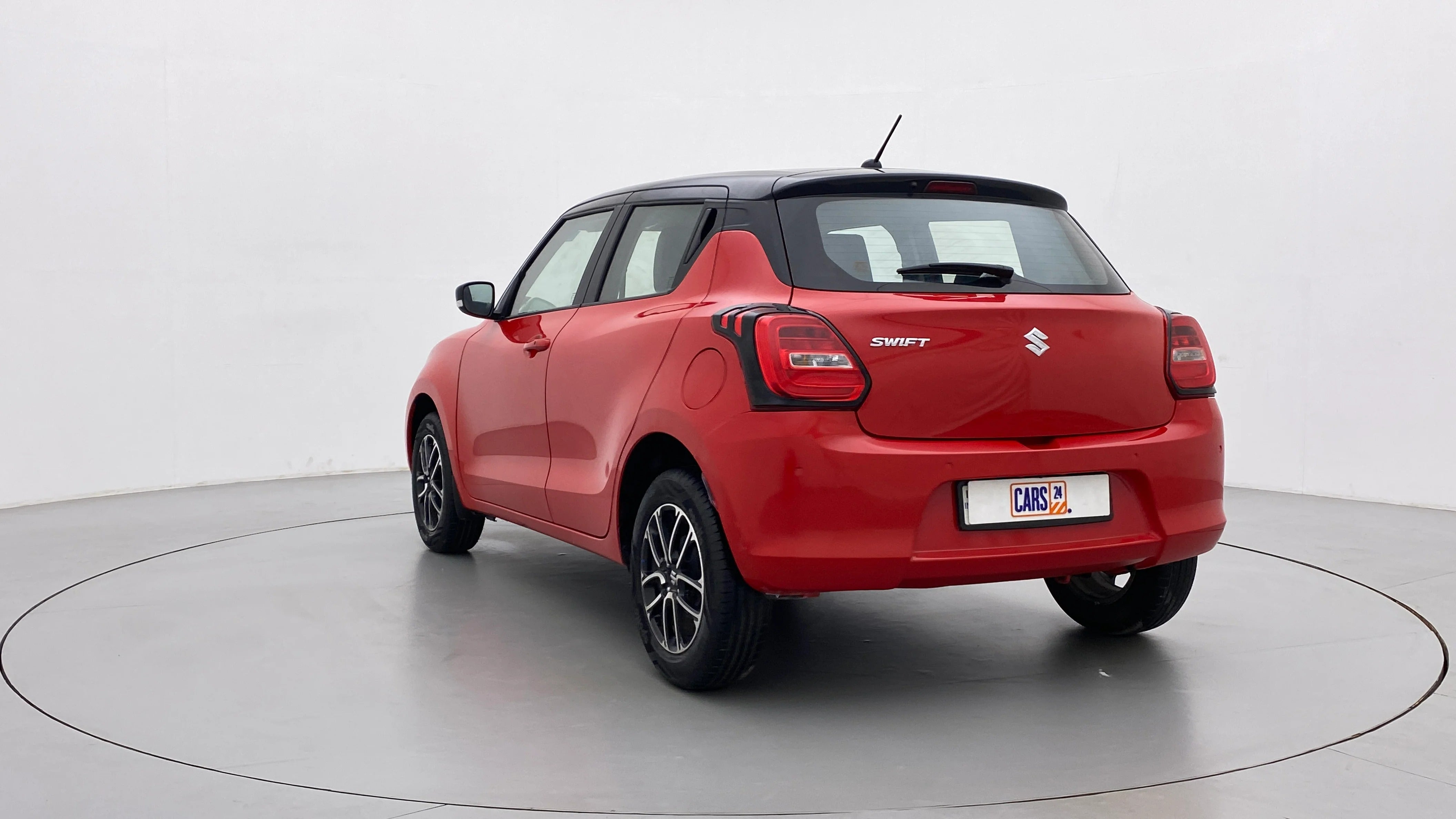 Rear three-quarter view of a solid fire red with pearl midnight black roof Maruti Suzuki Swift 2021 - 2023