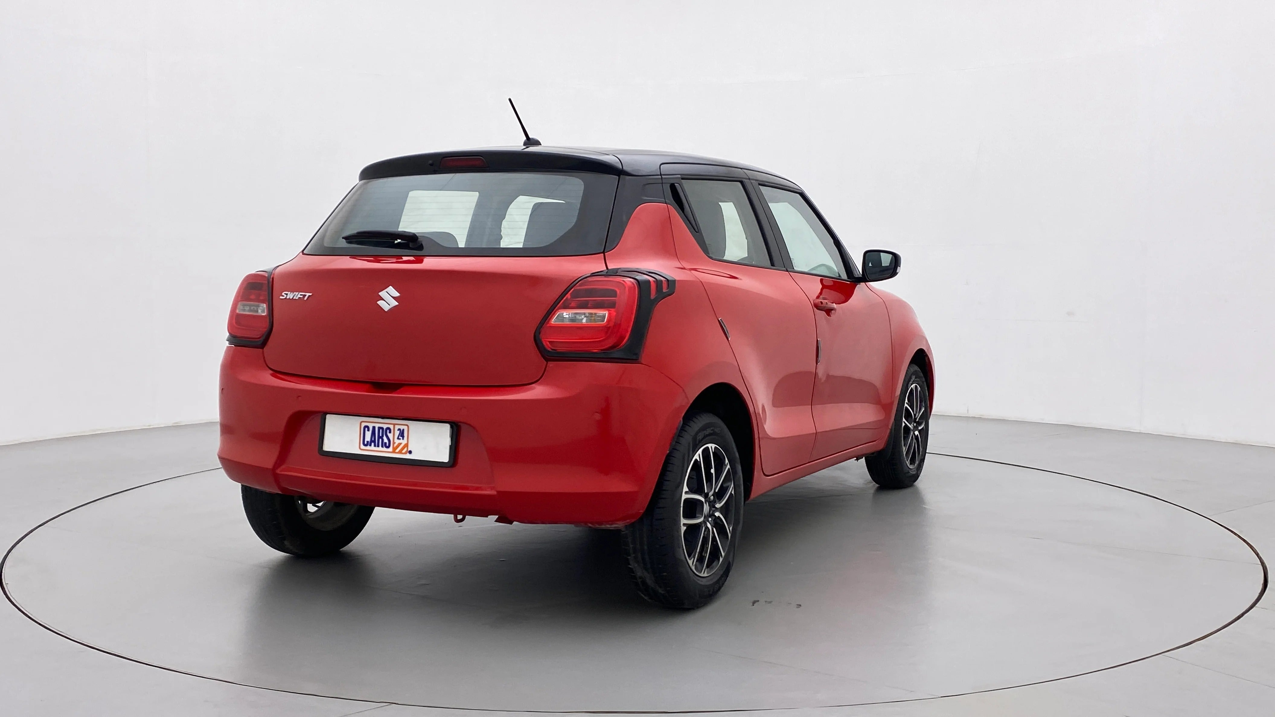 Rear three-quarter view of a solid fire red with pearl midnight black roof Maruti Suzuki Swift 2021 - 2023