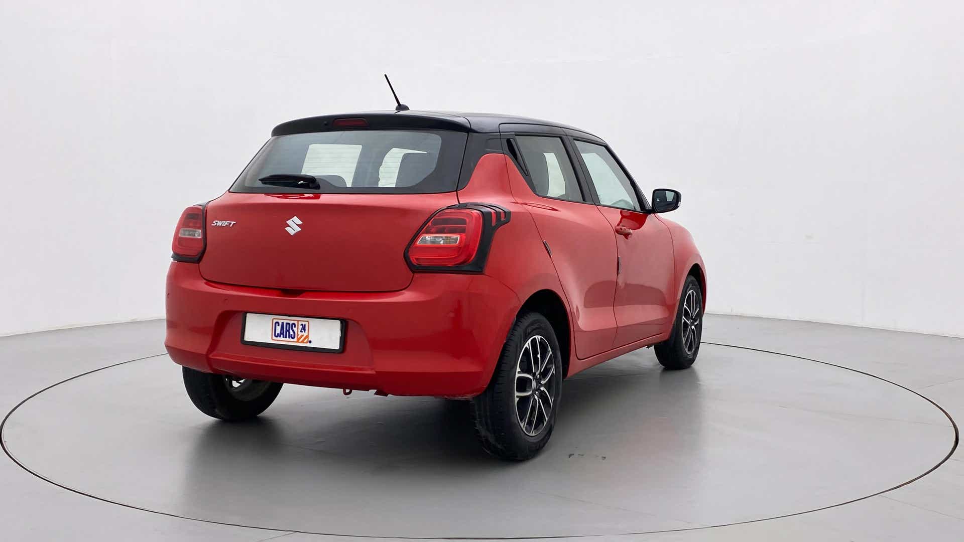 Rear three-quarter view of a solid fire red with pearl midnight black roof Maruti Suzuki Swift 2021 - 2023