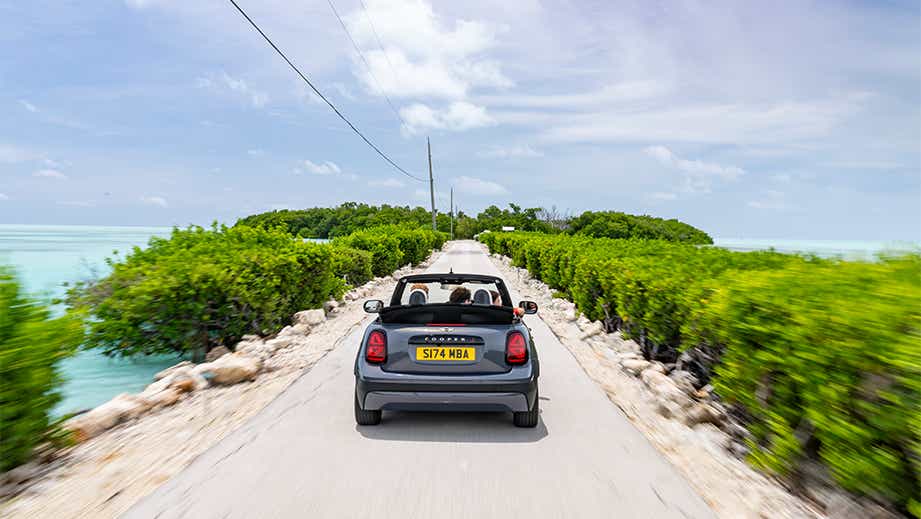 Rear view of a Mini Cooper S Convertible driving on a scenic road